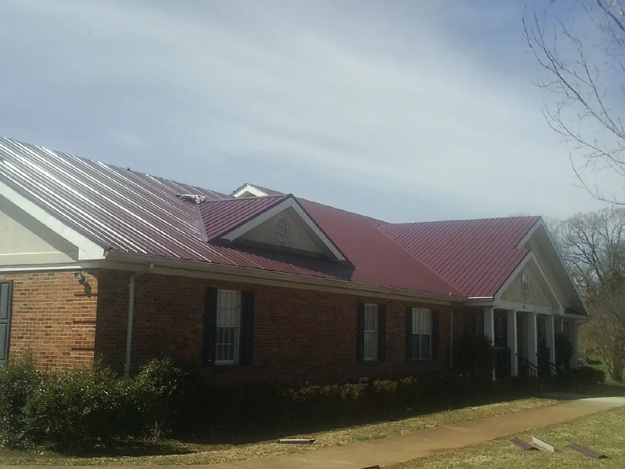 Red metal roof with gabled entries on a long brick building, from a Hail Damage Roof Repair job in Lawrence