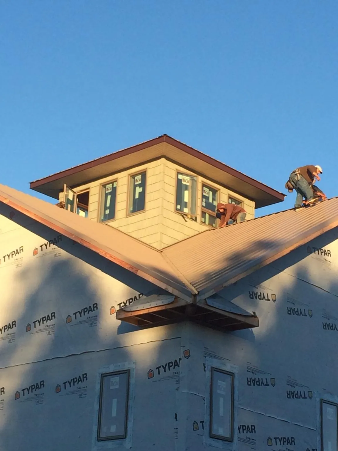 Roofers working around a rooftop cupola on a new metal roof at sunset — Roof Waterproofing in Lawrence by Roofing Brothers